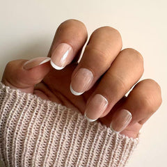 Classic glossy nude French tip press-on nails with short square shape displayed on female hands holding knitted fabric.