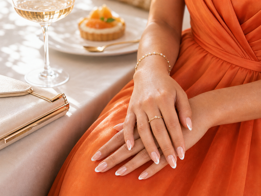 Nude French almond press-on nails styled with an orange wedding guest dress