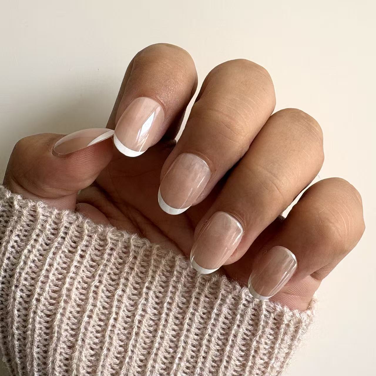 Classic glossy nude French tip press-on nails with short square shape displayed on female hands holding knitted fabric.