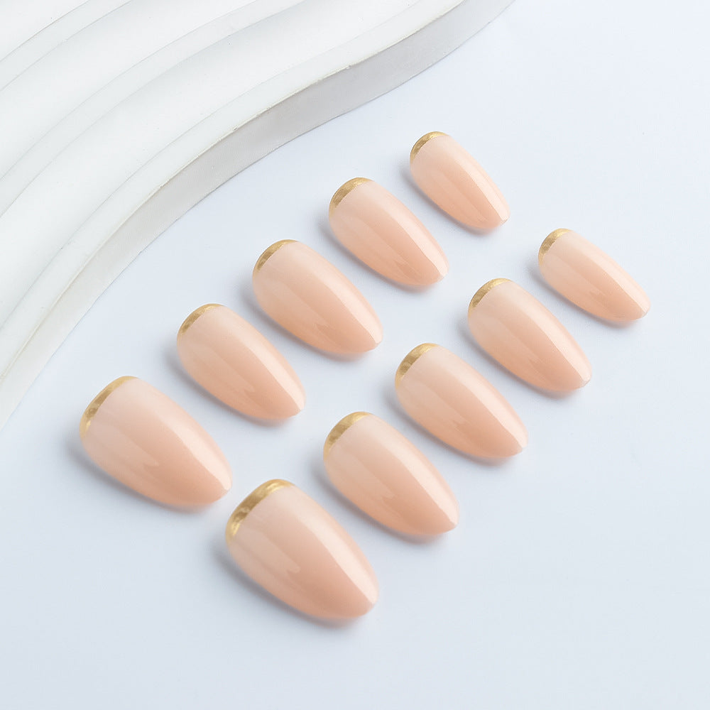 Luxury glossy nude almond press-on nails with elegant gold edge accents displayed on a hand model.