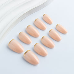 Luxury glossy nude almond press-on nails with elegant gold edge accents displayed on a hand model.