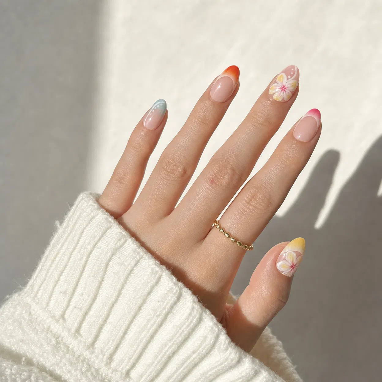 Hand with colorful nail art wearing a white sleeve and gold ring on a neutral background