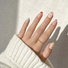 Hand with colorful nail art wearing a white sleeve and gold ring on a neutral background