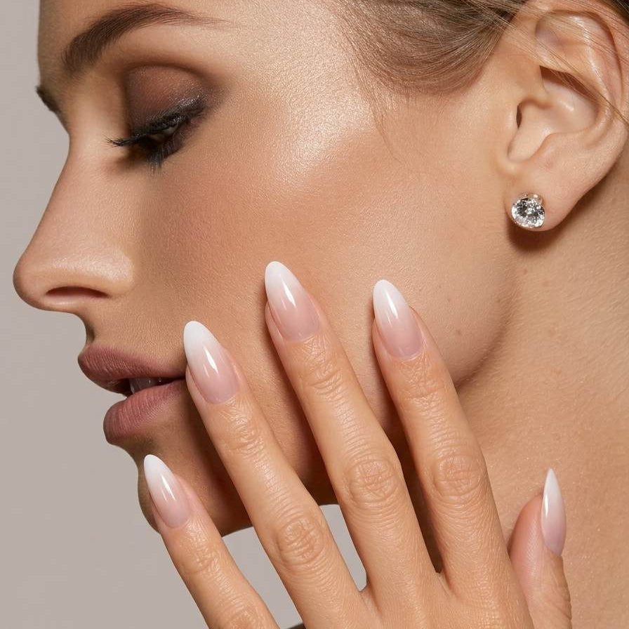 Close-up of a woman's face with a diamond earring and manicured nails against a neutral background